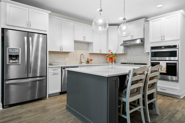 kitchen featuring a center island, light countertops, stainless steel appliances, and under cabinet range hood