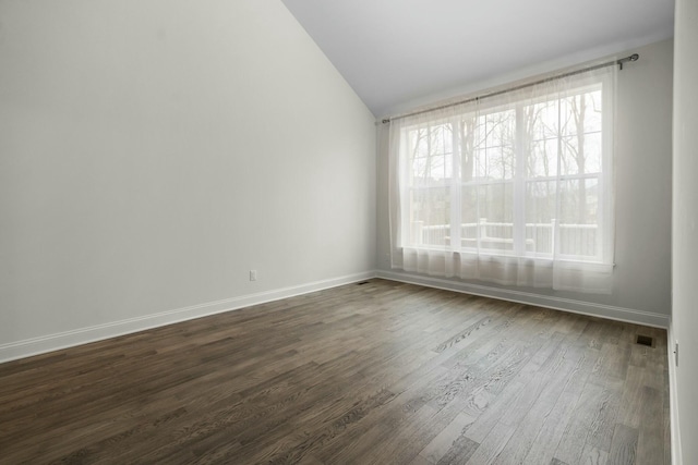 empty room with baseboards, visible vents, dark wood-type flooring, and vaulted ceiling