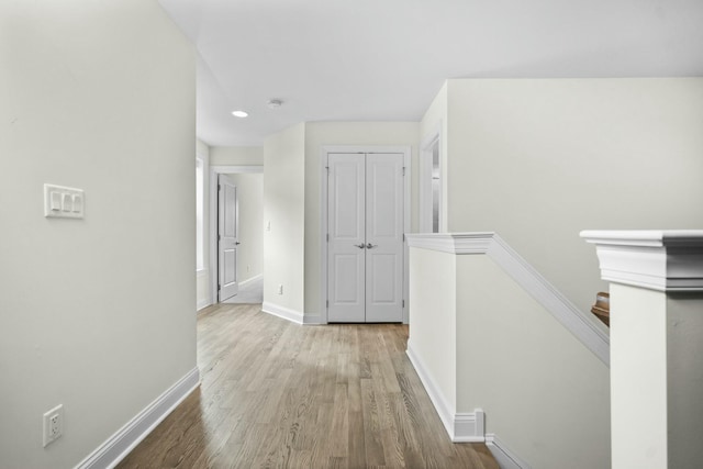 hallway featuring baseboards, recessed lighting, wood finished floors, and an upstairs landing