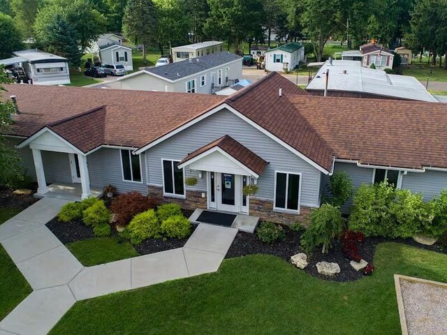 ranch-style house featuring a shingled roof, a front yard, and stone siding