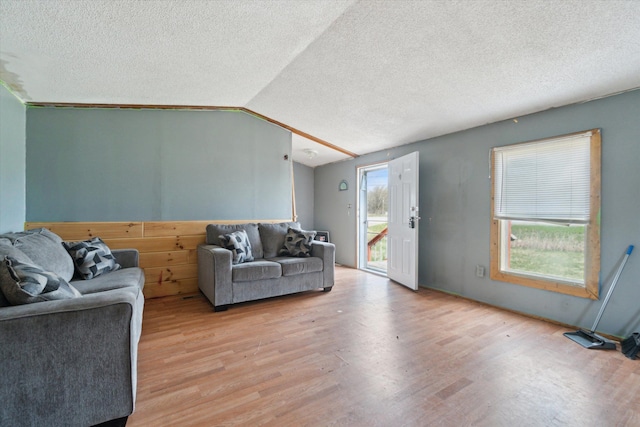 living room featuring a textured ceiling, light wood finished floors, and vaulted ceiling