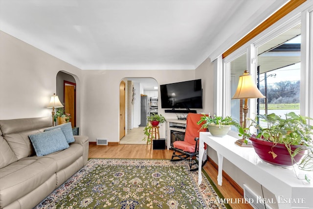 living room featuring baseboards, visible vents, arched walkways, and wood finished floors