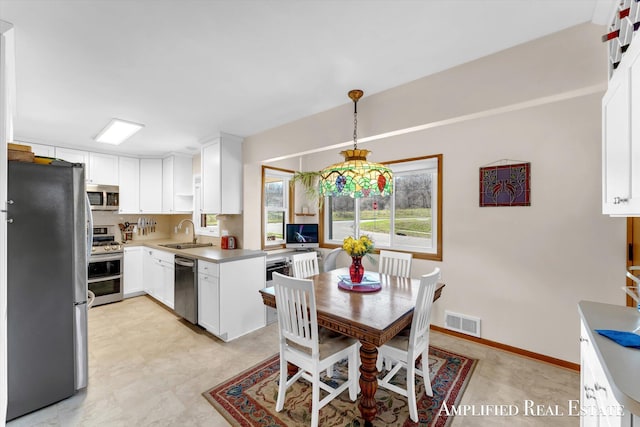 interior space featuring a sink, stainless steel appliances, visible vents, white cabinetry, and hanging light fixtures