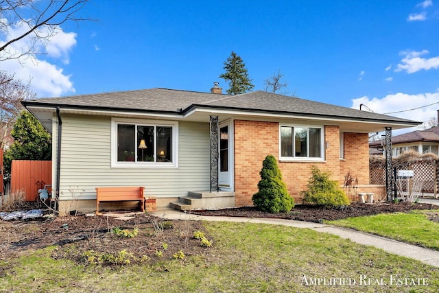 bungalow-style home featuring brick siding, fence, a front yard, and roof with shingles