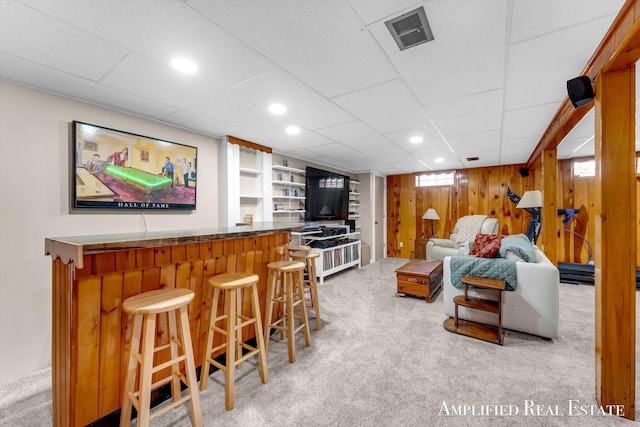 living room with visible vents, wood walls, light colored carpet, and a dry bar
