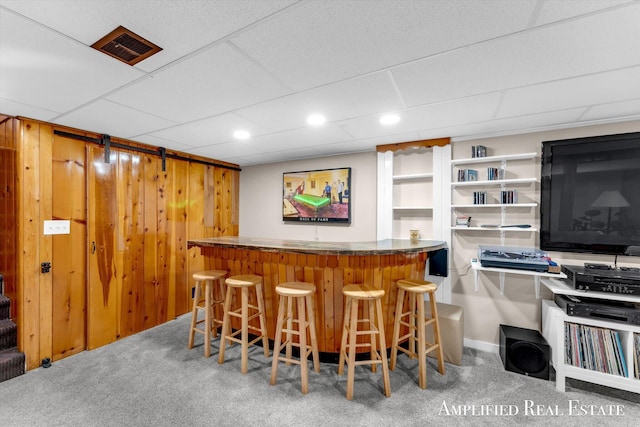 bar featuring carpet floors, wood walls, visible vents, a bar, and a paneled ceiling