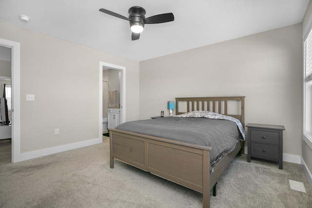 carpeted bedroom featuring multiple windows, ceiling fan, ensuite bath, and baseboards