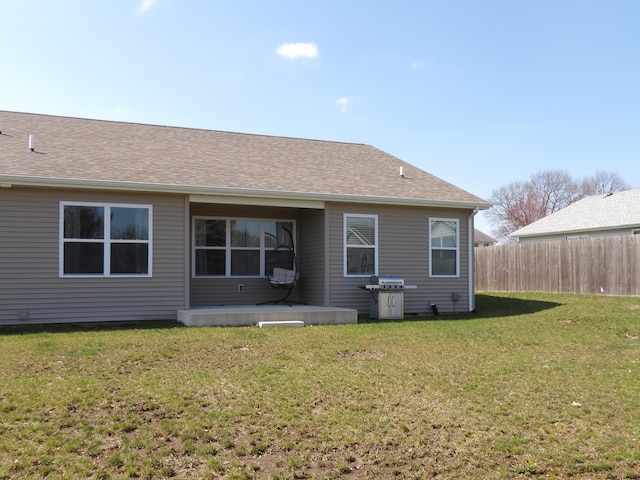 rear view of house with fence, roof with shingles, and a lawn