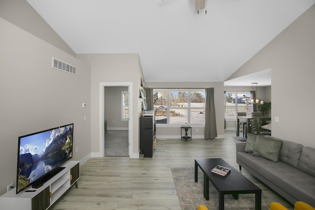 living area with a chandelier, light wood-style floors, vaulted ceiling, baseboards, and visible vents