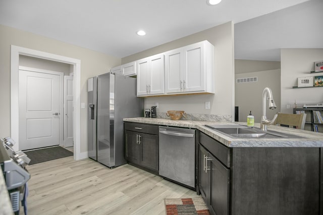 kitchen featuring stainless steel appliances, light countertops, light wood finished floors, white cabinetry, and a peninsula