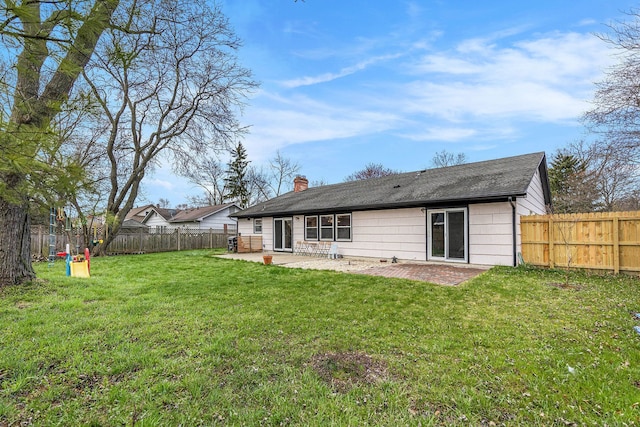 back of property with a chimney, roof with shingles, a lawn, a patio area, and a fenced backyard