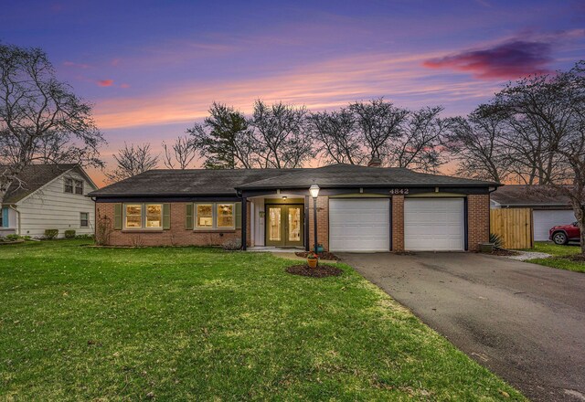 view of front of house featuring a lawn, french doors, brick siding, an attached garage, and driveway