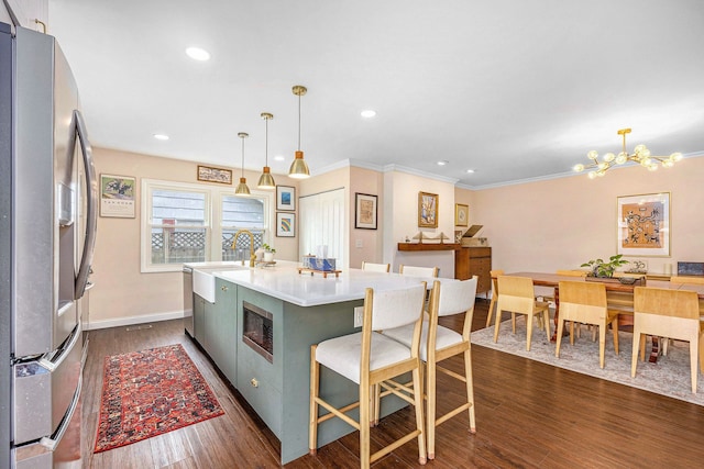 kitchen featuring appliances with stainless steel finishes, a sink, dark wood-style floors, ornamental molding, and an island with sink
