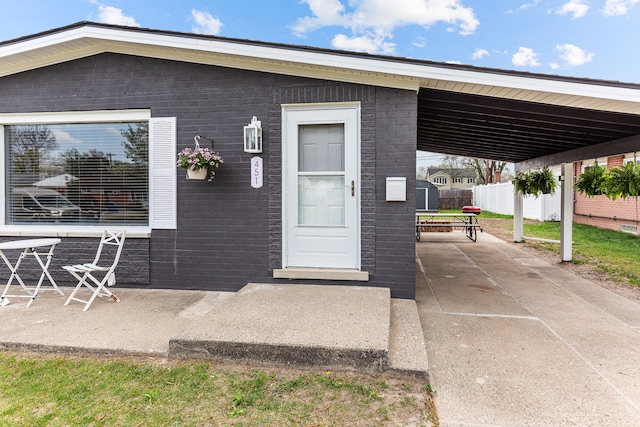 view of exterior entry with fence, a carport, and brick siding