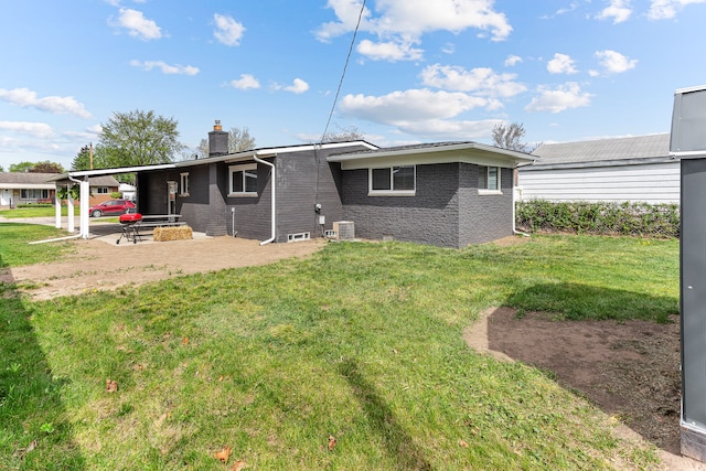 rear view of house with central AC, brick siding, a chimney, a lawn, and a patio