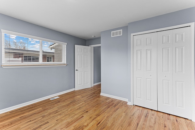 unfurnished bedroom with baseboards, visible vents, light wood finished floors, and a closet