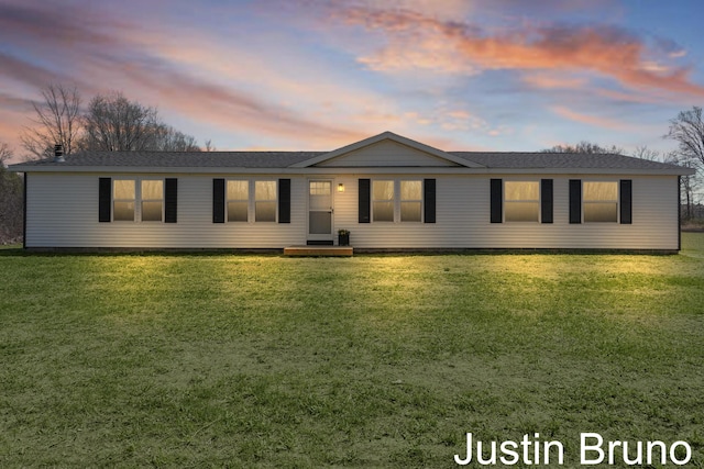 ranch-style home featuring a shingled roof and a yard