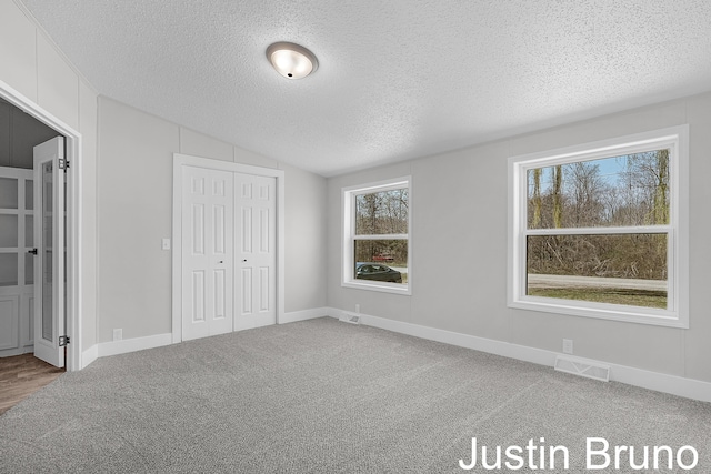 unfurnished bedroom with a textured ceiling, visible vents, multiple windows, and lofted ceiling