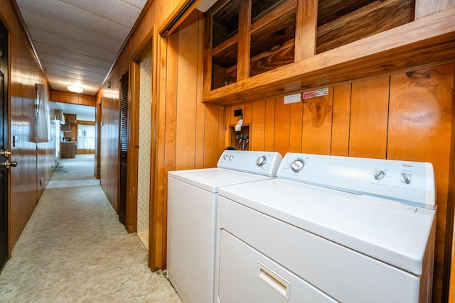 washroom with wood walls, washing machine and dryer, and light carpet