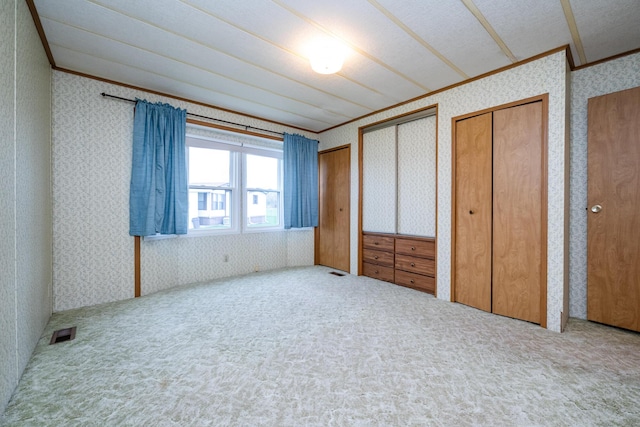 unfurnished bedroom with two closets, visible vents, carpet, ornamental molding, and wallpapered walls