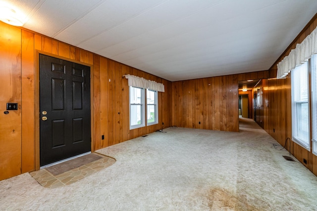foyer entrance with wooden walls, a healthy amount of sunlight, and carpet floors