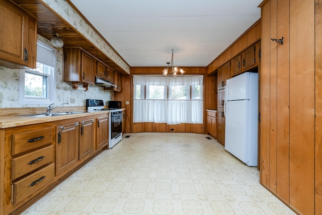 kitchen featuring white appliances, a wealth of natural light, under cabinet range hood, brown cabinets, and a sink