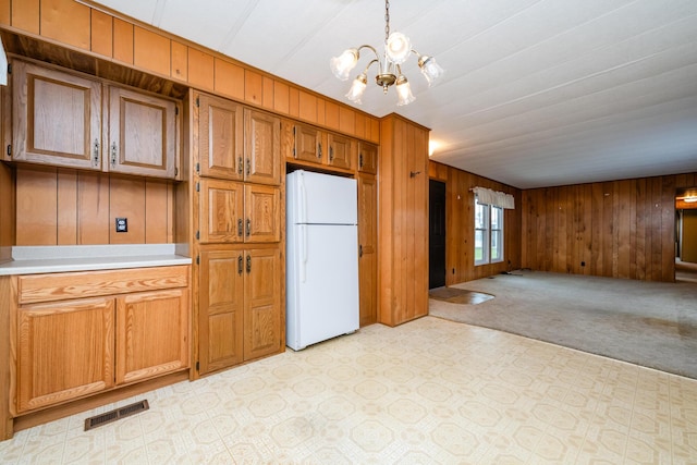 kitchen with visible vents, wood walls, a notable chandelier, and freestanding refrigerator