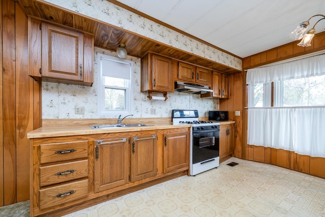 kitchen with wallpapered walls, under cabinet range hood, light countertops, a sink, and range with gas stovetop