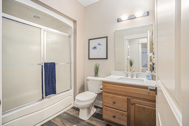 full bath with combined bath / shower with glass door, wood finished floors, toilet, and vanity