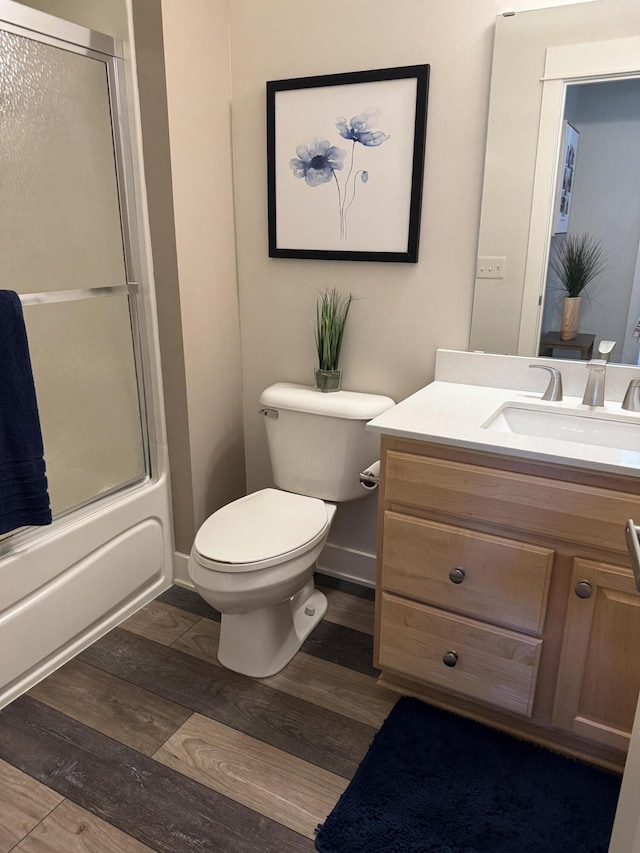full bathroom featuring wood finished floors, toilet, vanity, baseboards, and bath / shower combo with glass door