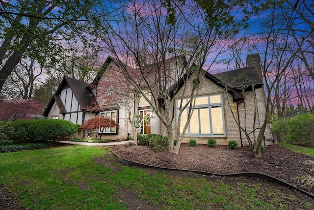 rear view of property featuring a chimney, brick siding, and a yard