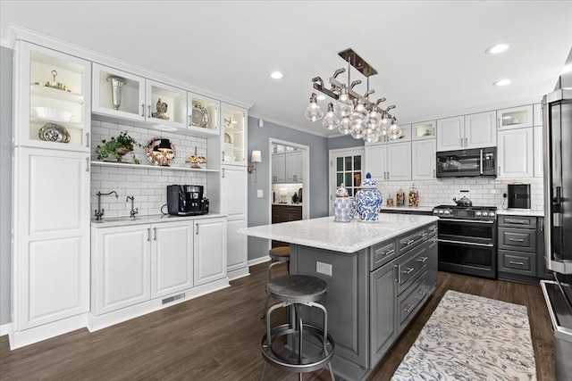 kitchen with black microwave, double oven range, white cabinetry, dark wood-type flooring, and decorative backsplash