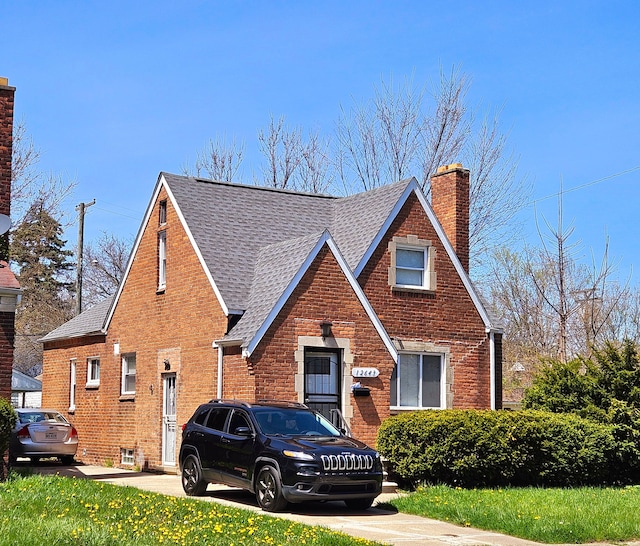 tudor-style house with a chimney, a shingled roof, and brick siding