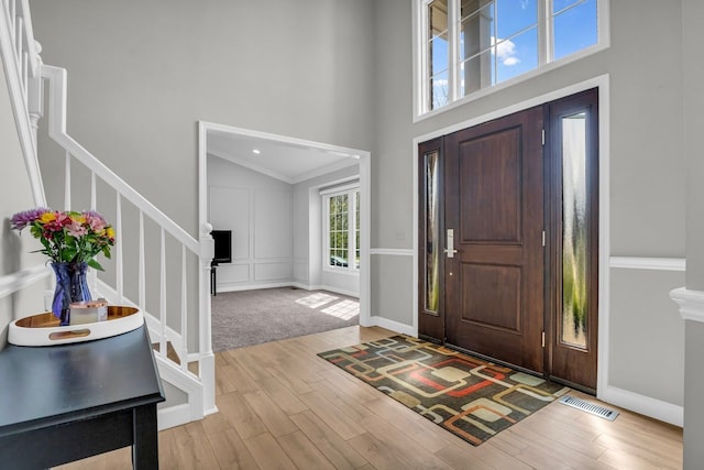 foyer entrance featuring wood finished floors, visible vents, a high ceiling, and stairs