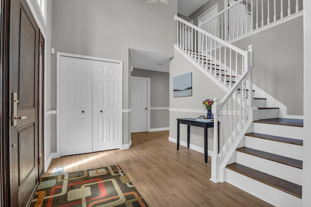 entryway with stairway, wood finished floors, baseboards, and a high ceiling