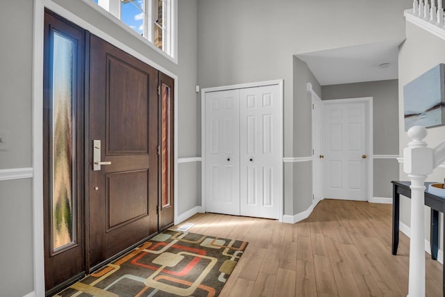 entrance foyer with baseboards, a wealth of natural light, light wood-style floors, and a towering ceiling