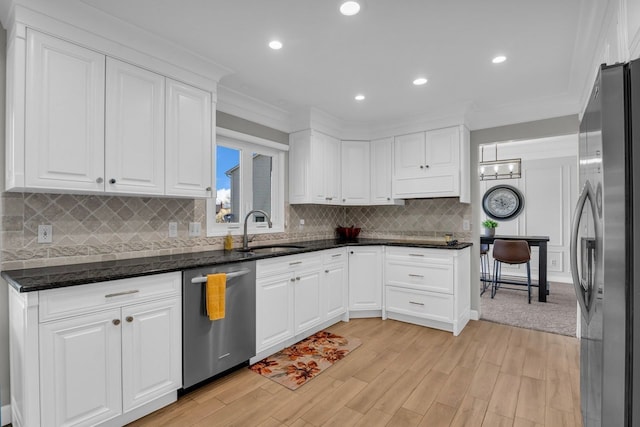 kitchen with white cabinetry, decorative backsplash, a sink, appliances with stainless steel finishes, and light wood finished floors