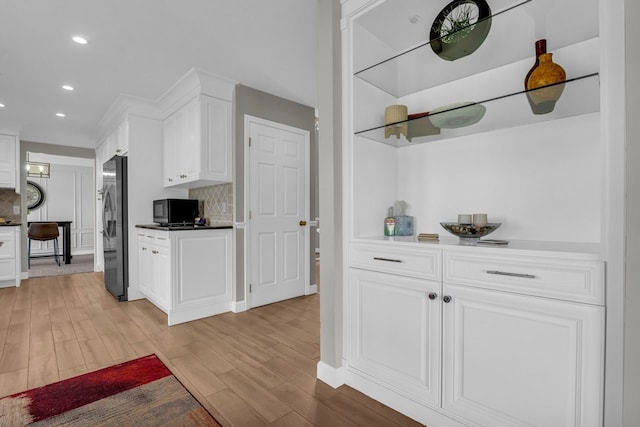 kitchen featuring stainless steel microwave, light wood finished floors, decorative backsplash, white cabinetry, and freestanding refrigerator