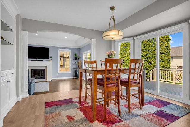dining area featuring ornate columns, wood finished floors, a healthy amount of sunlight, and arched walkways