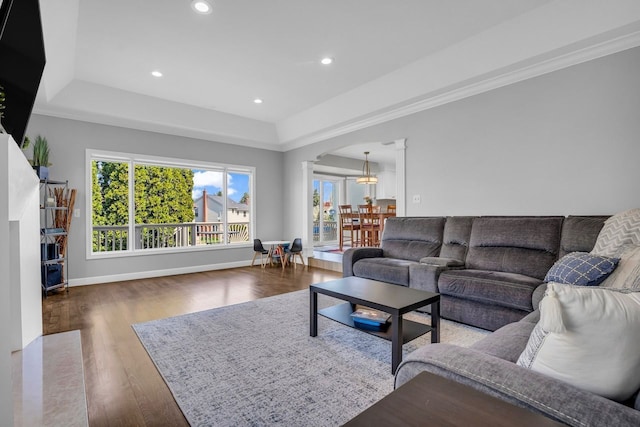 living area with baseboards, arched walkways, wood finished floors, and a tray ceiling