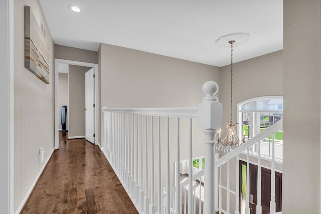 hallway featuring wood finished floors, a notable chandelier, and baseboards