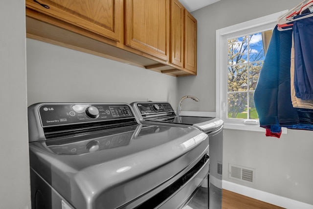 laundry area with visible vents, baseboards, washer and dryer, cabinet space, and wood finished floors