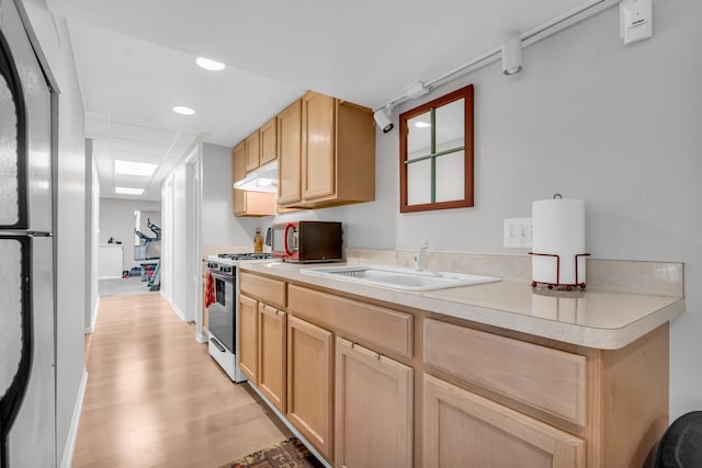kitchen with stainless steel microwave, a sink, under cabinet range hood, white range with gas cooktop, and light wood-style flooring