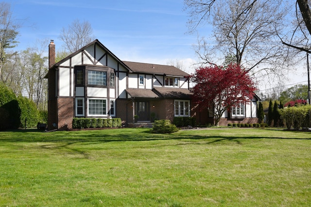 rear view of house featuring a yard, brick siding, a chimney, and stucco siding