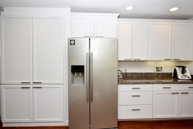 kitchen featuring stainless steel fridge, dark stone counters, and white cabinets