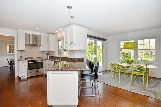 kitchen with electric range, a peninsula, wall chimney exhaust hood, white cabinetry, and a sink