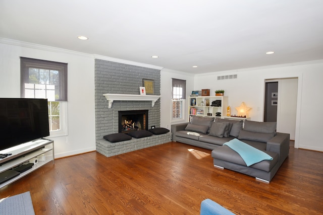 living room featuring visible vents, ornamental molding, a brick fireplace, wood finished floors, and baseboards