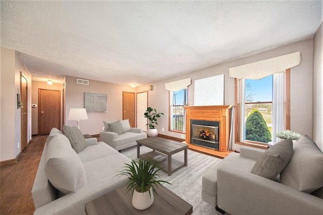 living area with visible vents, wood finished floors, a textured ceiling, and a fireplace with flush hearth