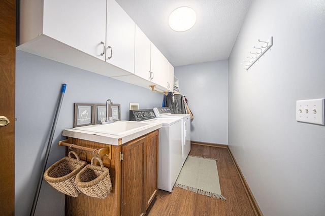 clothes washing area with light wood-style flooring, a sink, baseboards, washer and dryer, and cabinet space