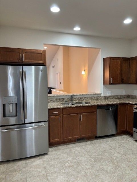 kitchen featuring light tile patterned flooring, recessed lighting, light stone counters, a sink, and appliances with stainless steel finishes